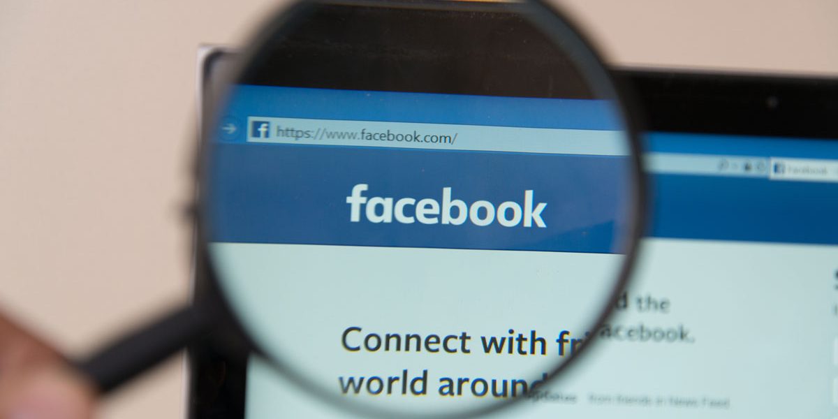 Someone holding up a magnifying glass to the Facebook website