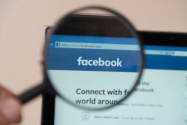 Someone holding up a magnifying glass to the Facebook website